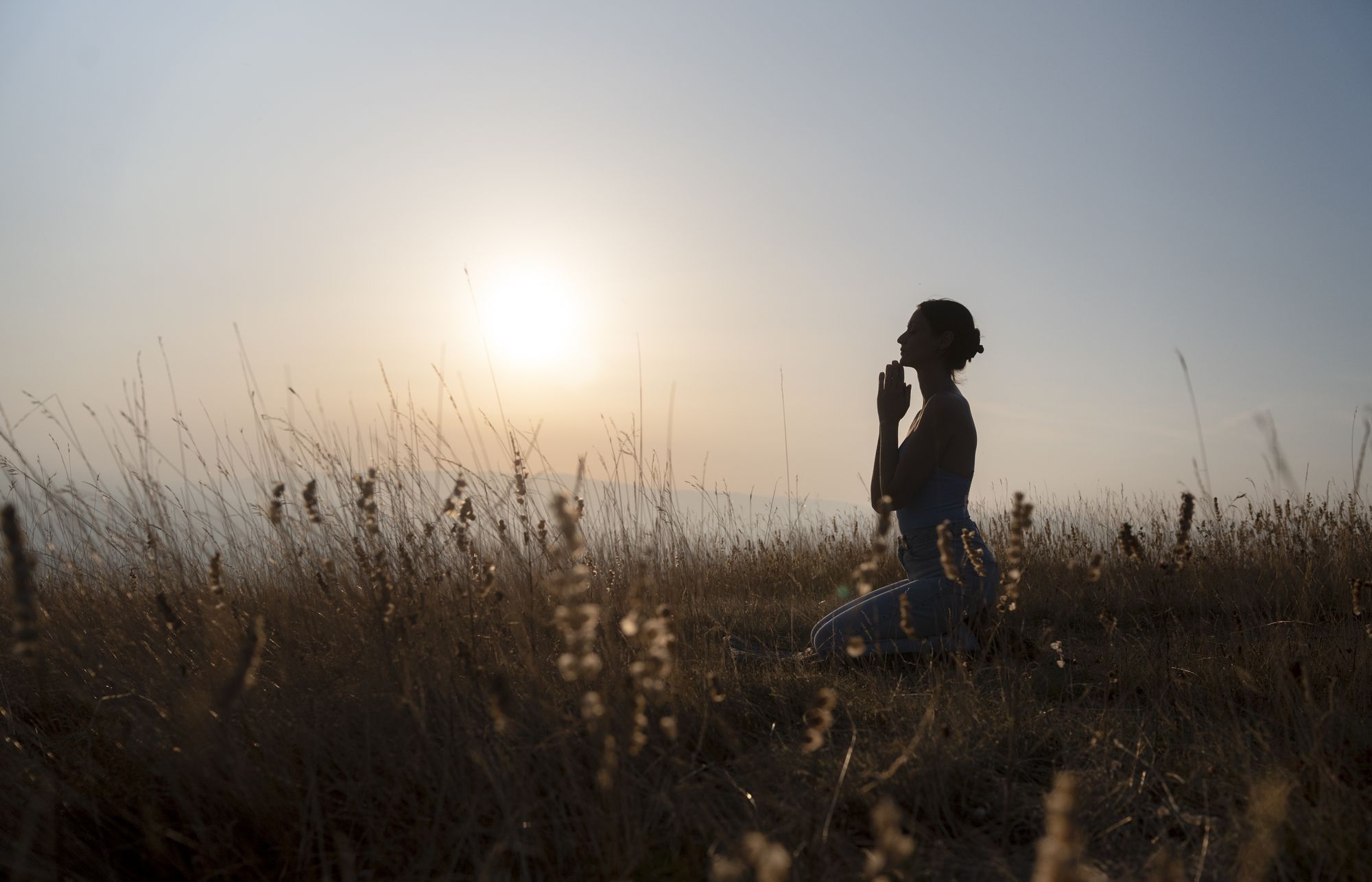 A woman kneeling in prayer in a golden field at dawn