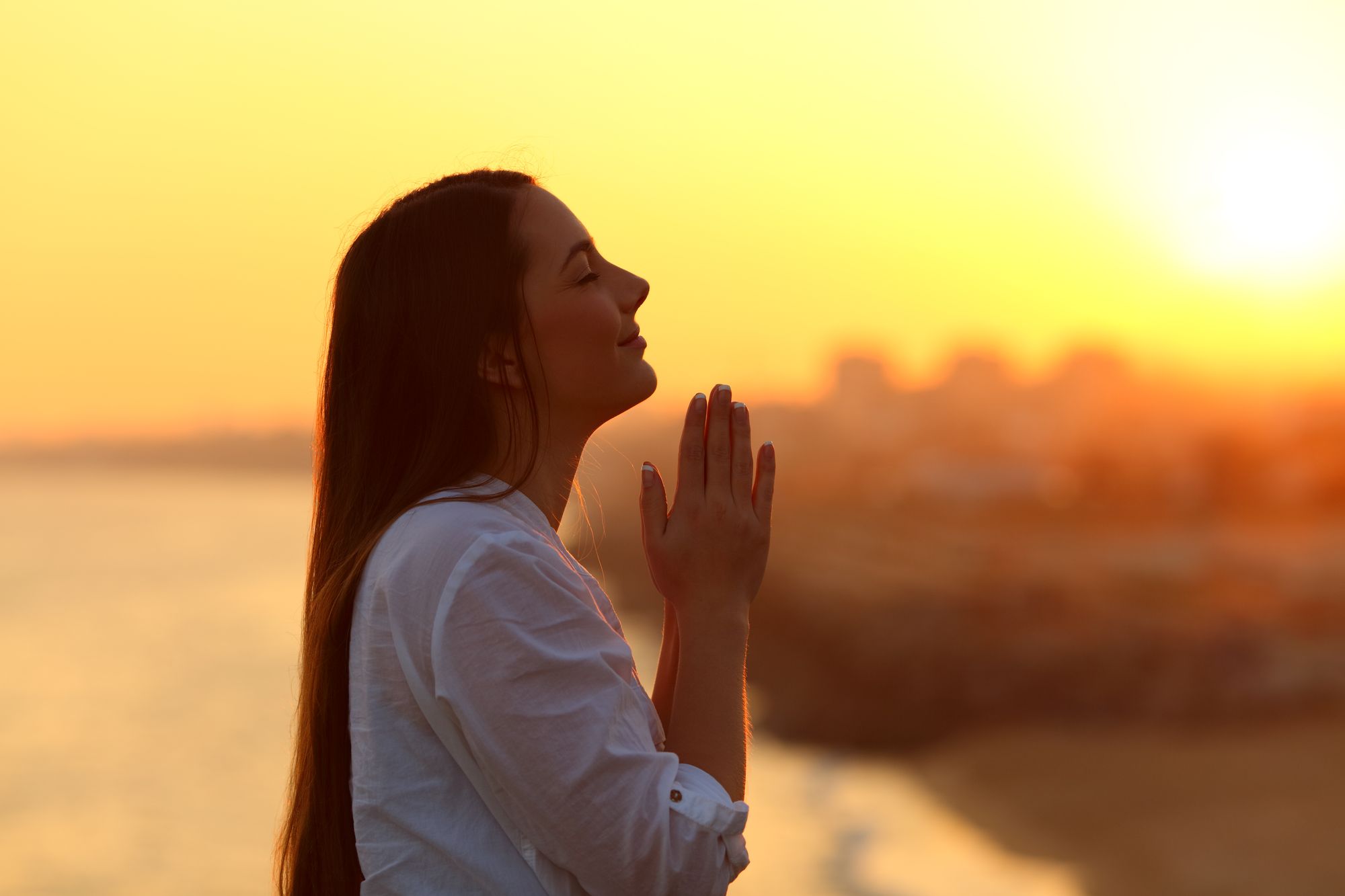 A woman praying at sunset by the sea